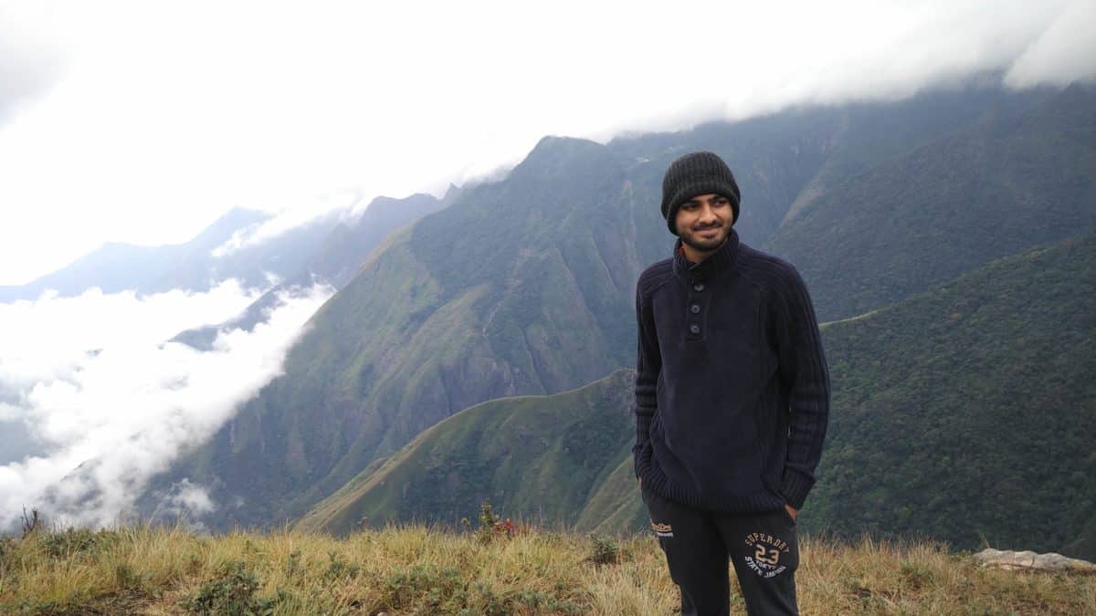 Teja standing in front of a deep, cloudy valley and mountains in Munnar, India.
