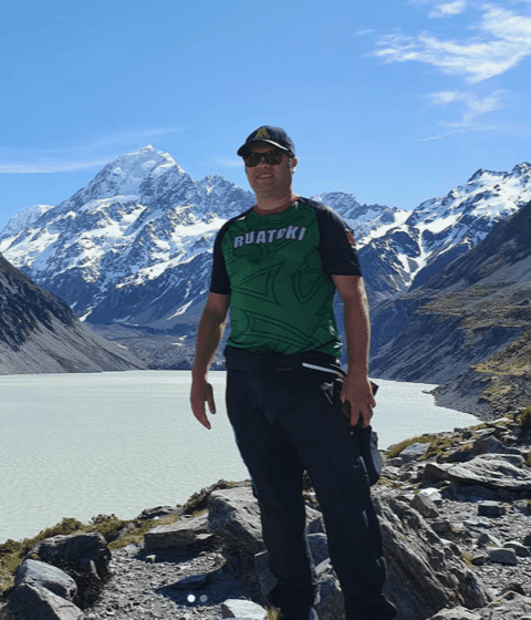 Tamati standing in front of a glacial lake, glacier and snow-capped mountains.